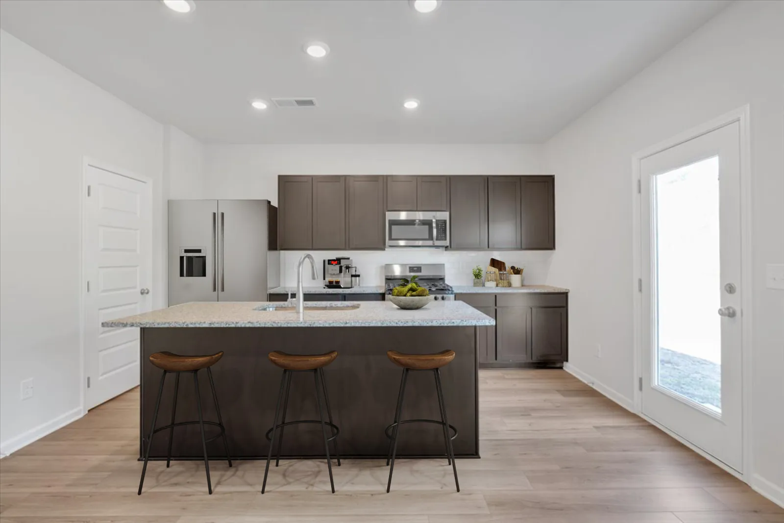 Modern kitchen with gray cabinets, granite island, stainless steel appliances, and wooden bar stools on light wood floor