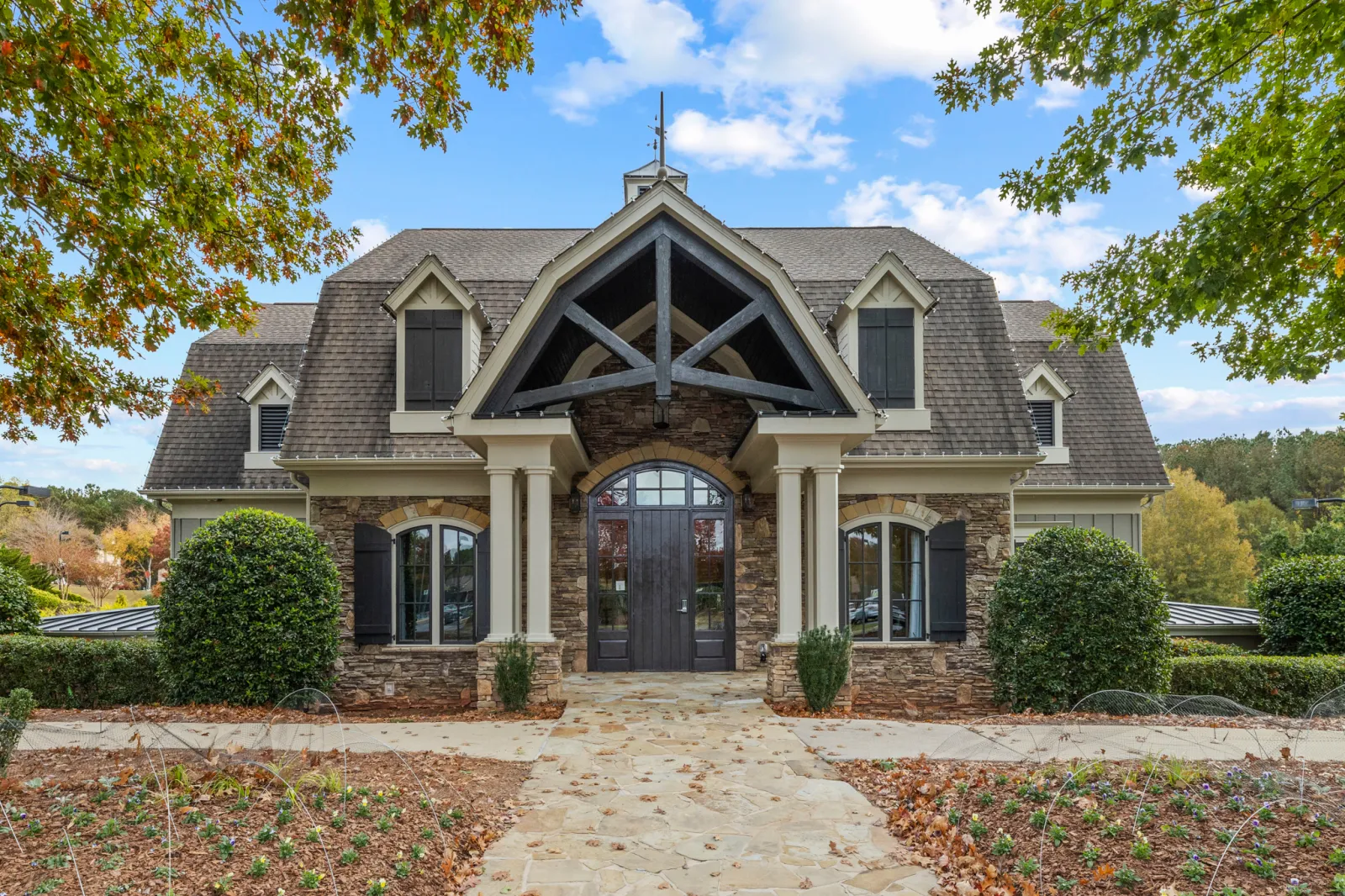 Stone and wood craftsman-style house with arched doorway, dormer windows, and landscaped front yard on a clear day.