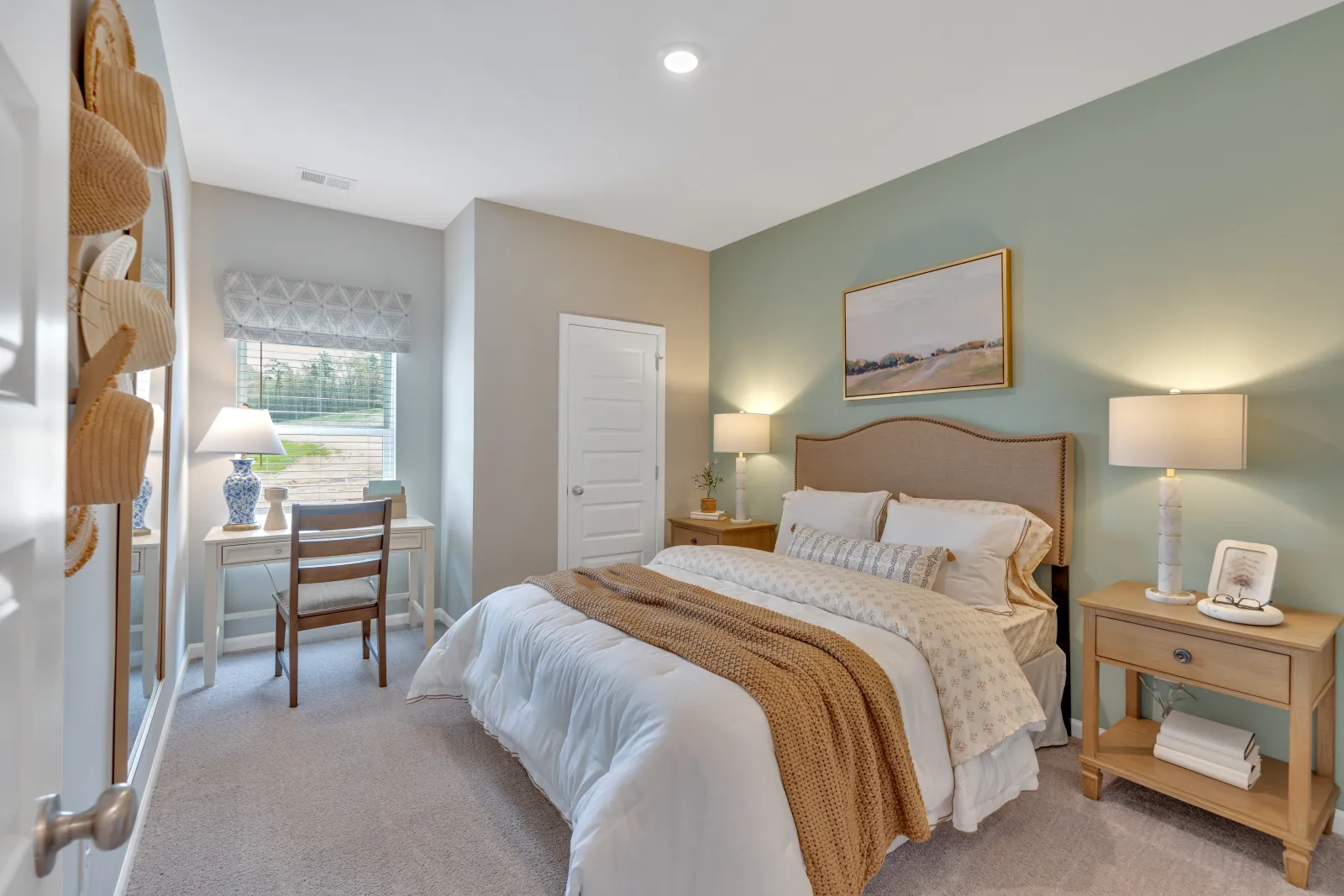 Cozy bedroom with a bed, desk, and natural light, featuring soft colors and stylish decor.