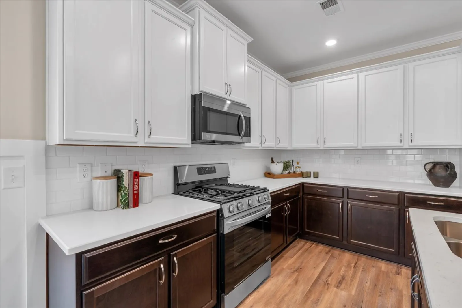 Modern kitchen with white upper cabinets, dark lower cabinets, stainless steel appliances, and wood flooring.