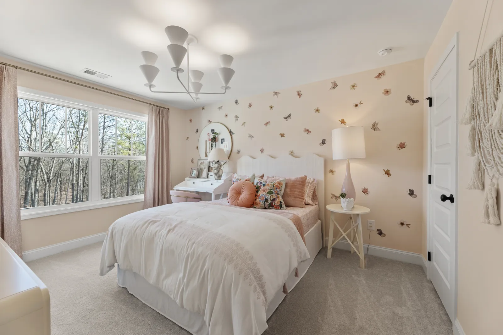 Cozy bedroom with white bed, floral pillows, butterfly wall decals, large window, and modern chandelier light fixture.
