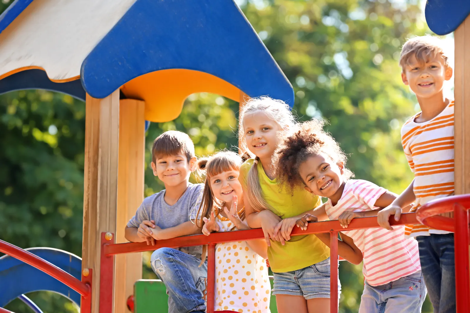 Group of diverse children smiling and playing together on colorful playground equipment outdoors.