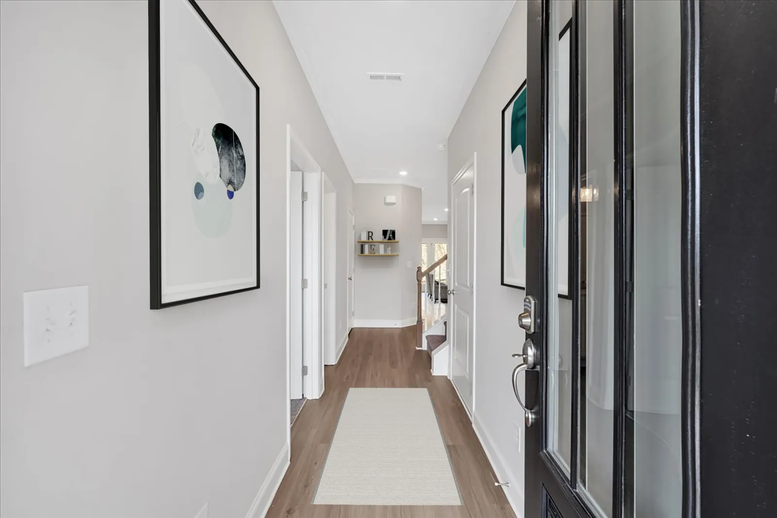 Modern home entryway with wooden floor, white walls, abstract wall art, and a black front door.