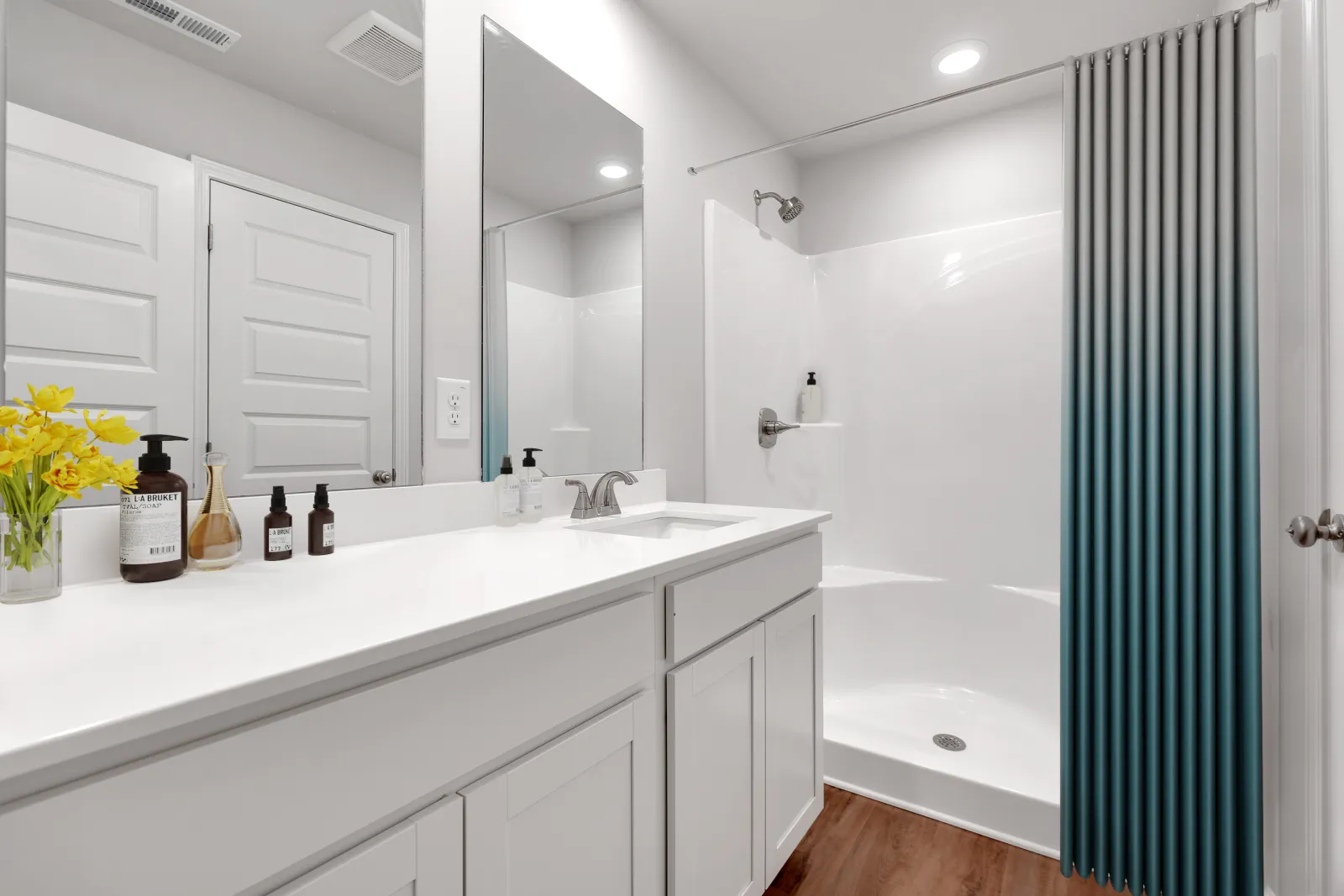 Bright modern bathroom with white vanity, large mirror, walk-in shower, and wood-look flooring