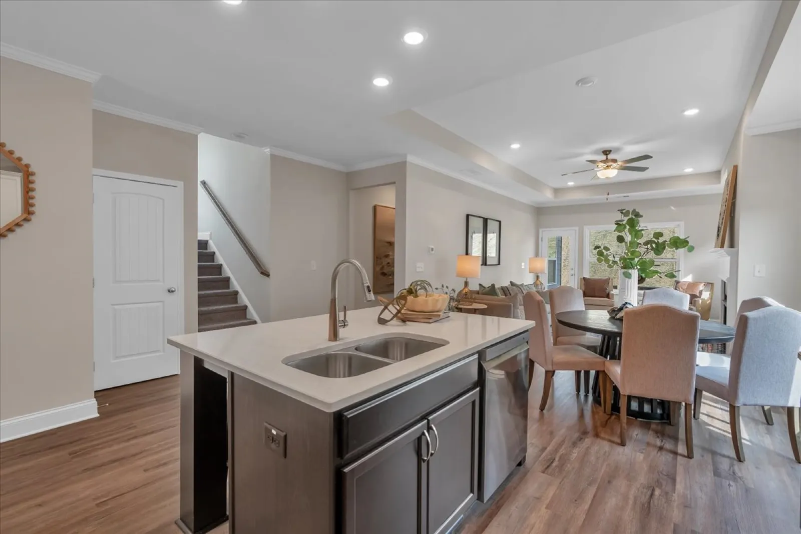 Modern kitchen island with sink, stainless steel dishwasher, and adjacent dining area with chairs and ceiling fan.