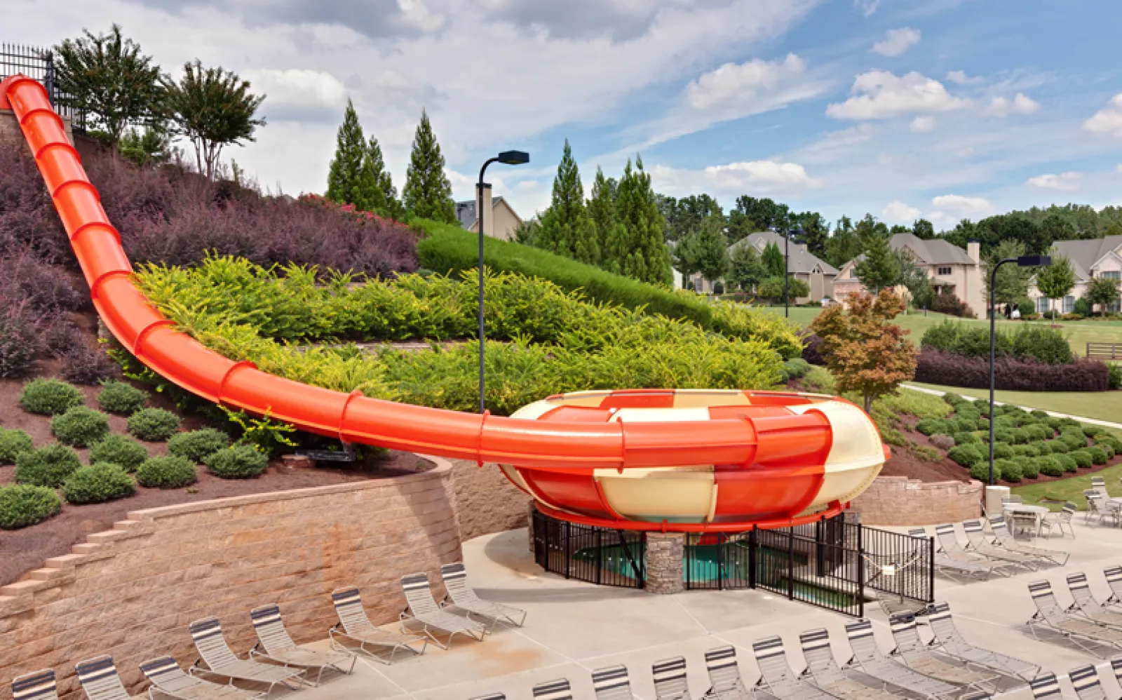 Large orange and white water slide with funnel shape at the bottom surrounded by lounge chairs and greenery.