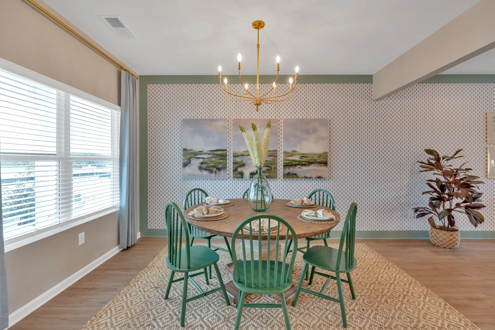 Stylish dining room featuring a round green table, chairs, chandelier, and decorative wall art.