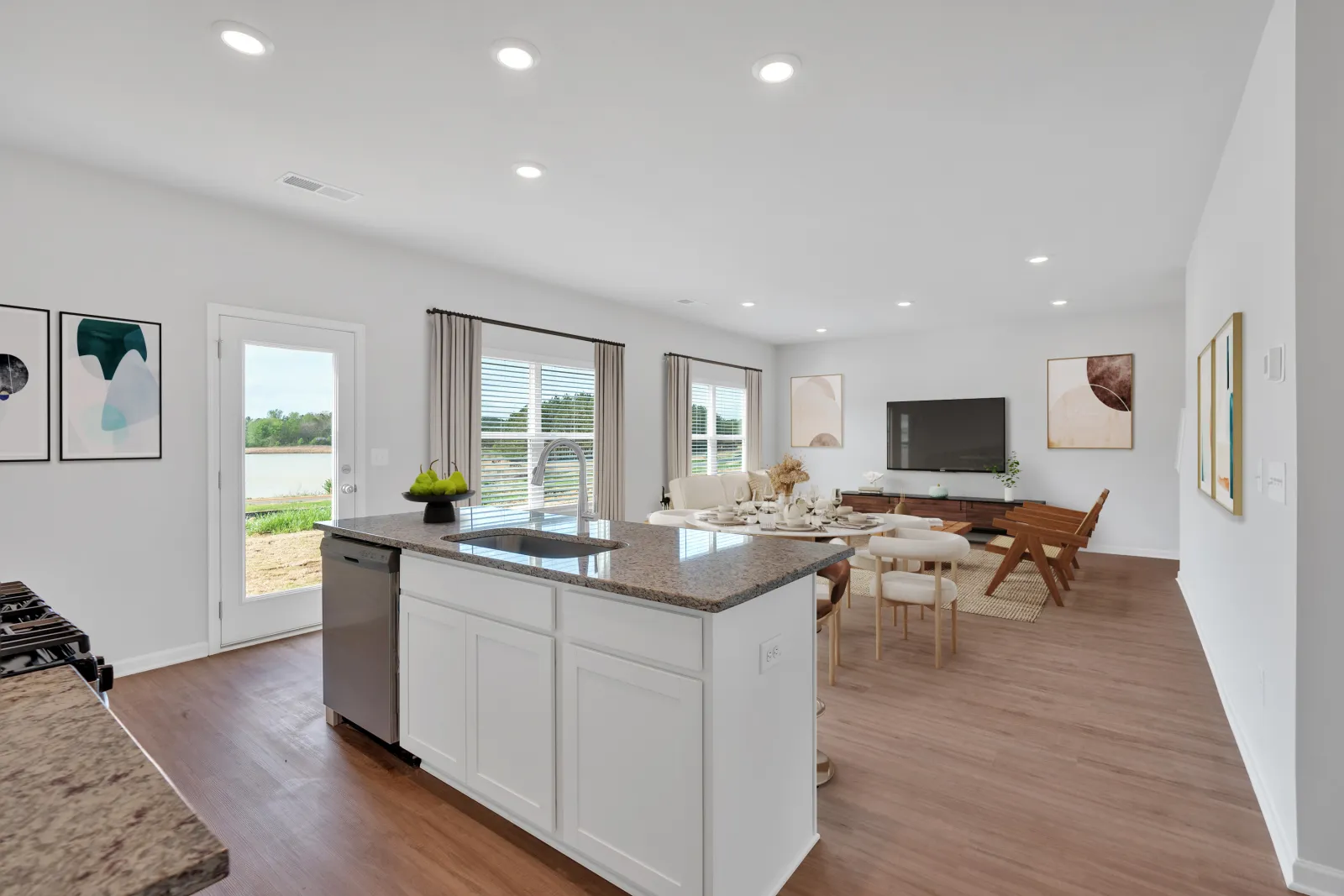 Bright open-concept kitchen and living room with white cabinetry, granite countertops, and modern wood flooring.