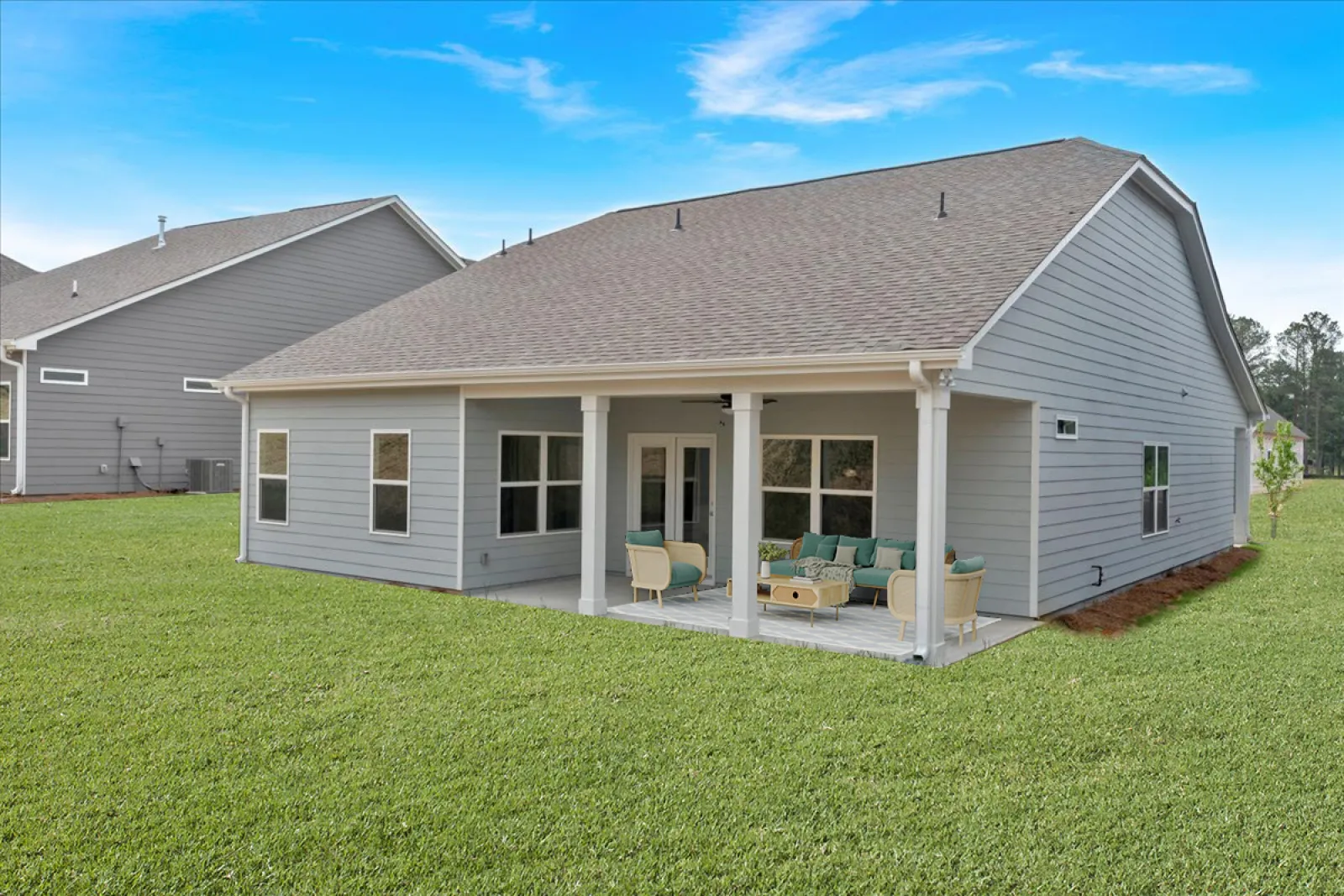 Modern gray house with covered patio, outdoor furniture, and a green lawn under a blue sky.