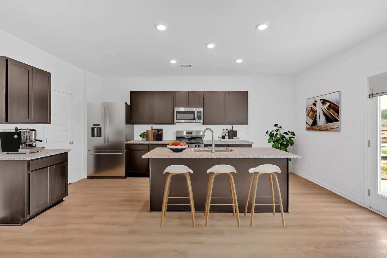 Modern kitchen with dark wood cabinets, stainless steel appliances, an island with three stools, and light hardwood floors.