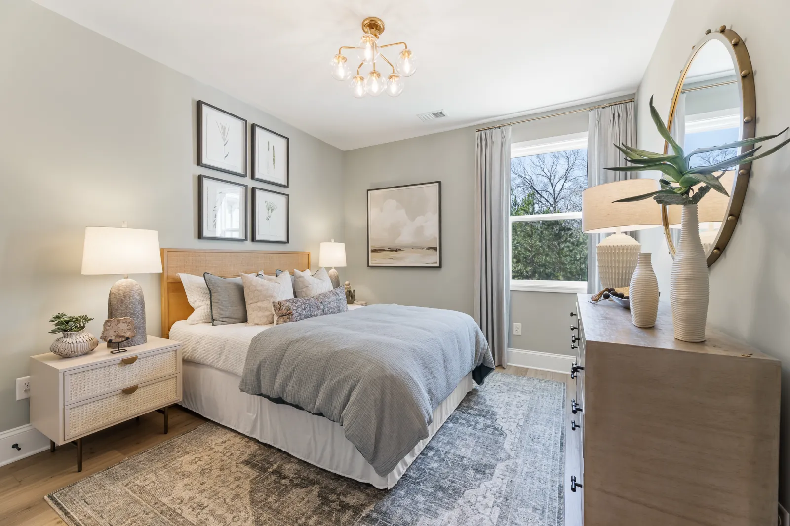 Cozy bedroom with gray bedding, wooden furniture, soft lighting, decorative wall art, and a large window with curtains