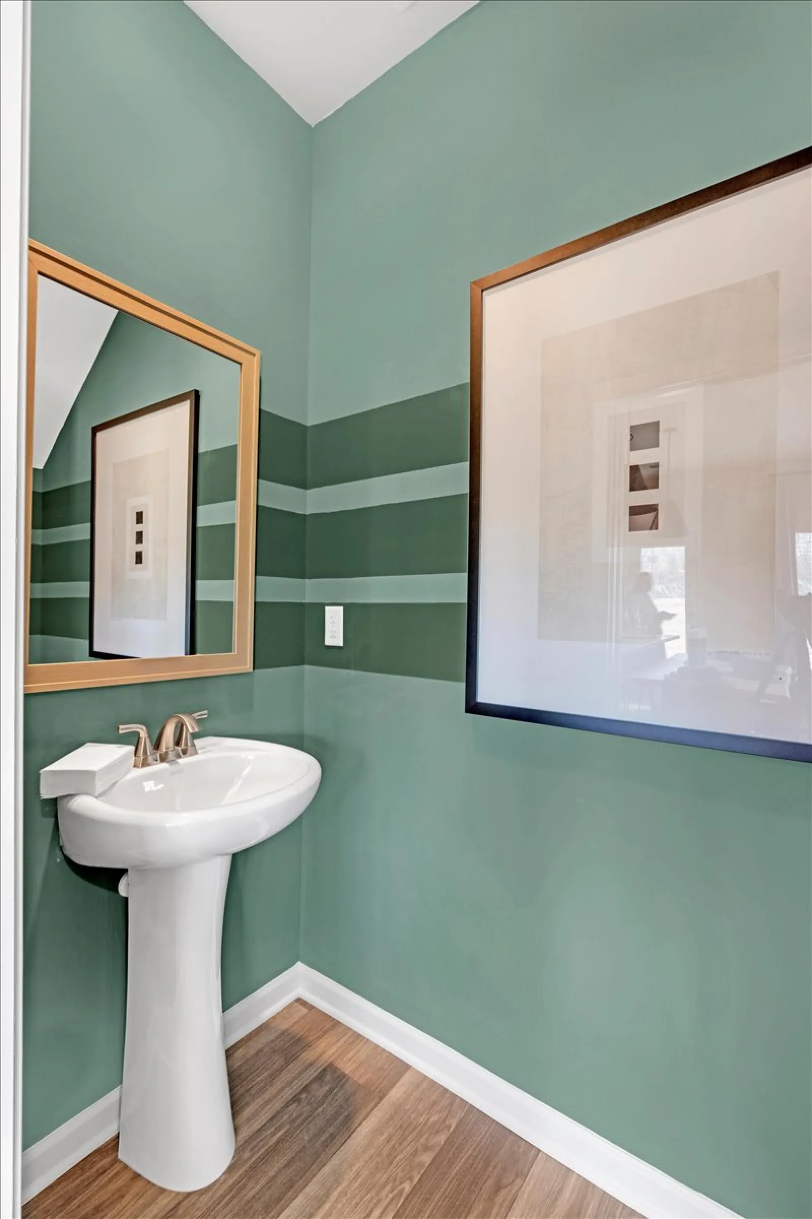 Elegant green bathroom with modern sink, framed artwork, and stylish striped walls.