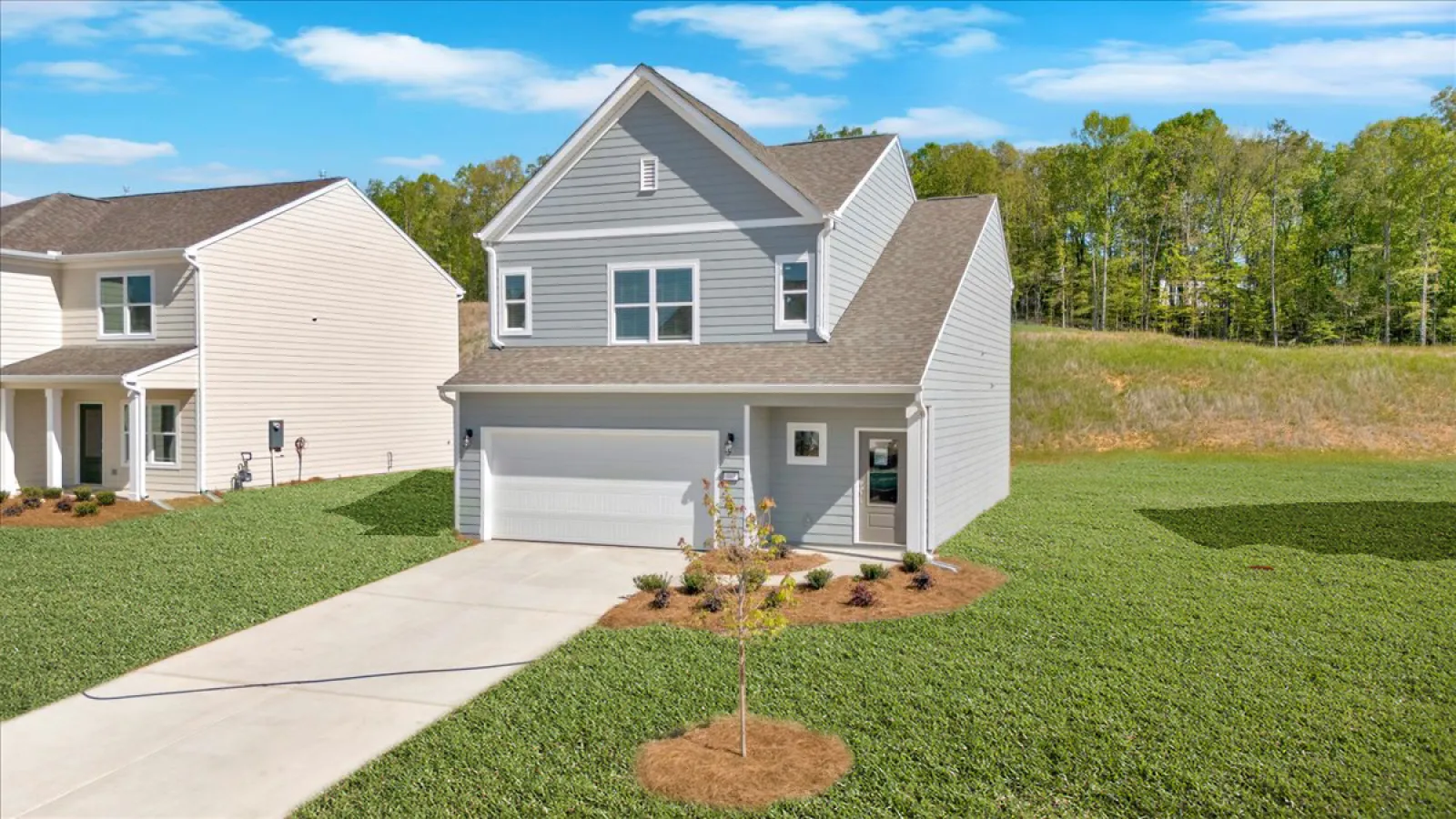Modern two-story gray house with attached garage, landscaped front yard, and clear blue sky background.