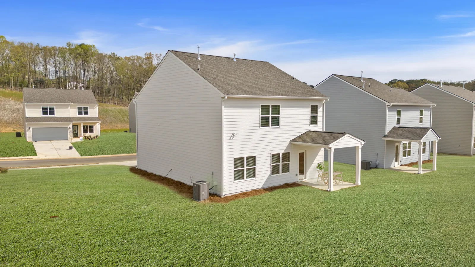 Suburban two-story white houses with spacious green lawns under a clear blue sky