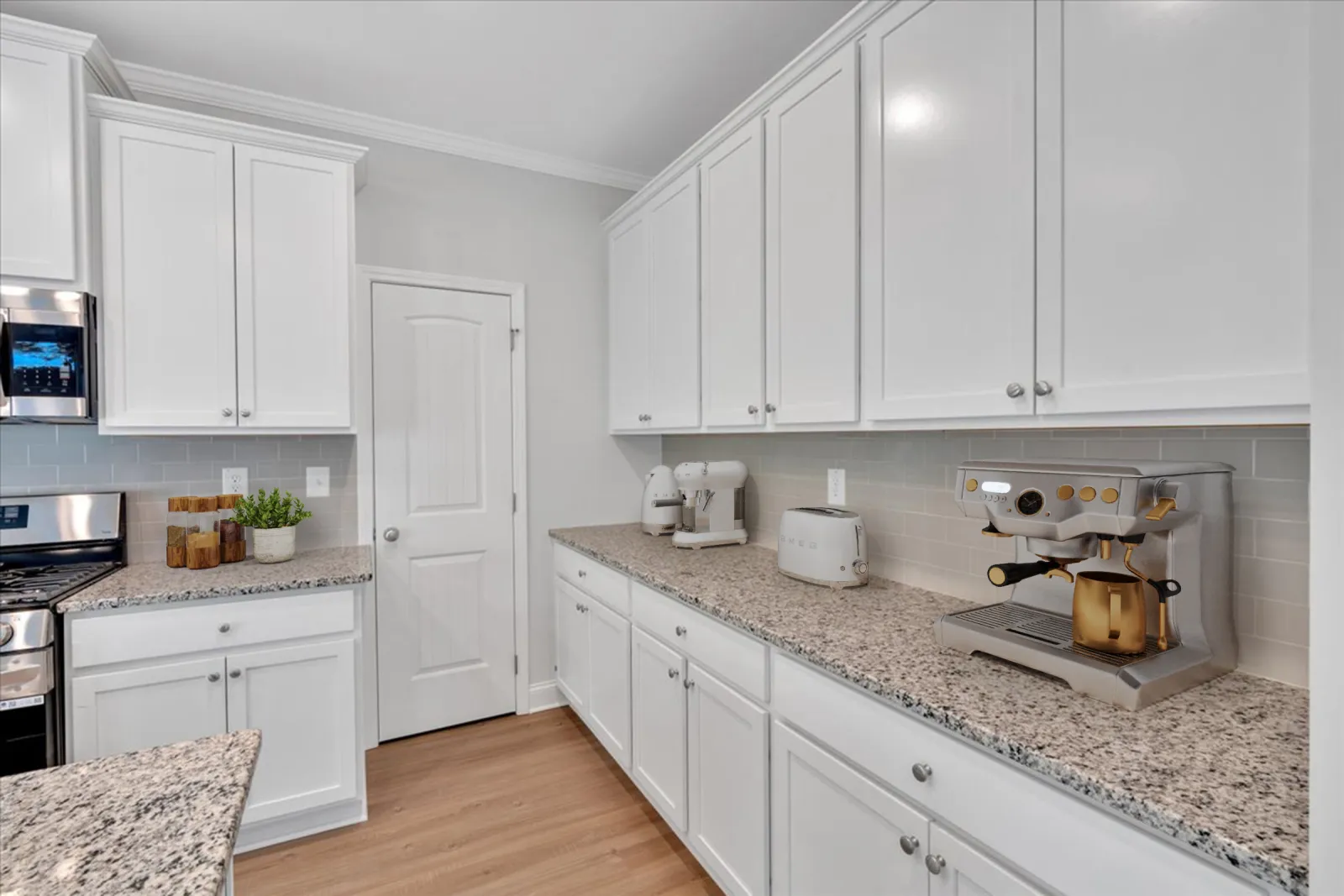 Modern kitchen with white cabinets, granite countertops, espresso machine, toaster, and hardwood flooring.