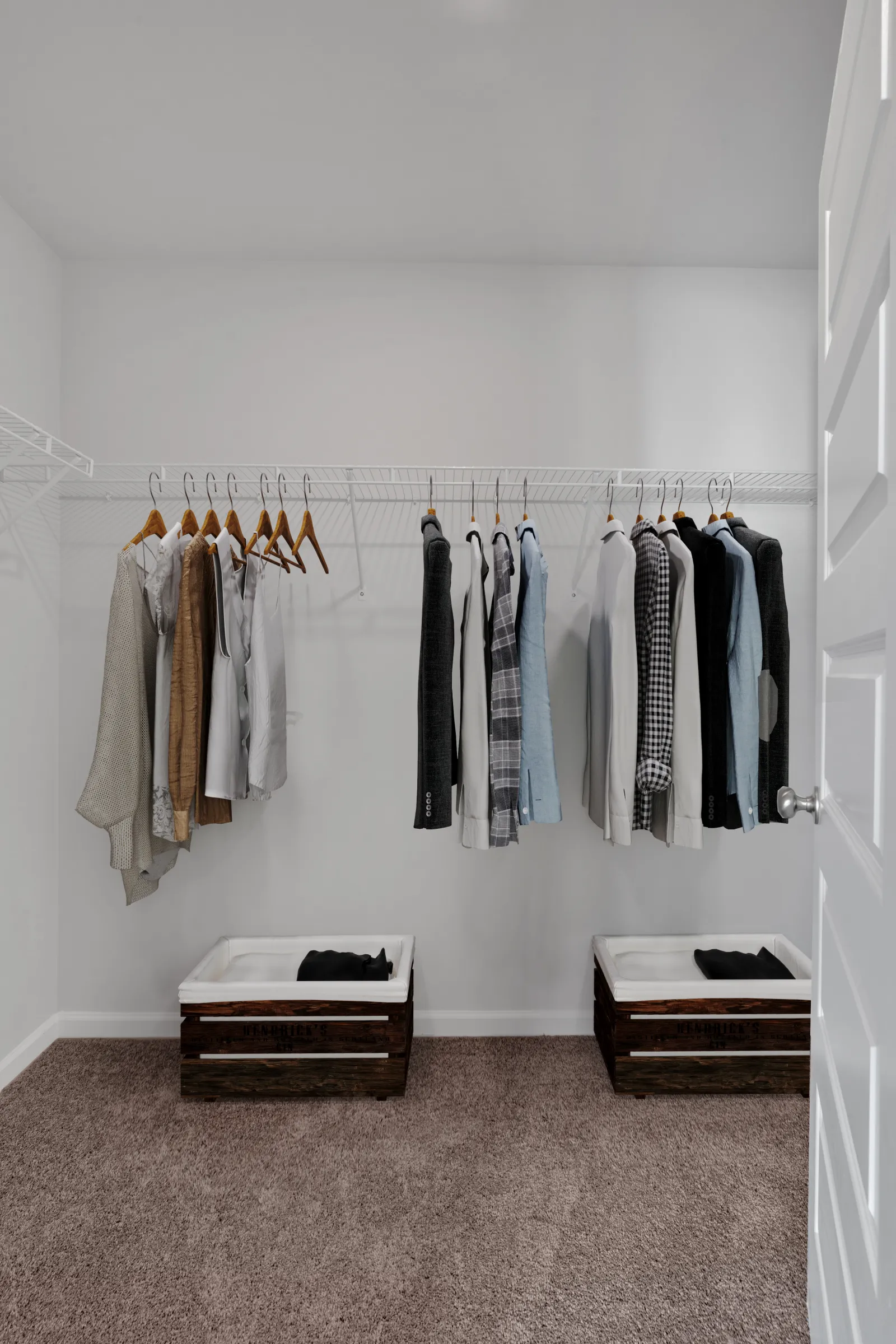 Minimalist closet with hanging neutral-toned clothes and two wooden storage bins on carpeted floor.