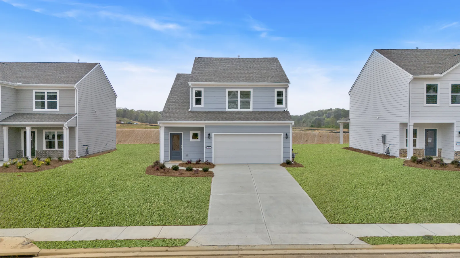 Modern homes with gray siding and driveways, surrounded by green lawns under a clear blue sky.