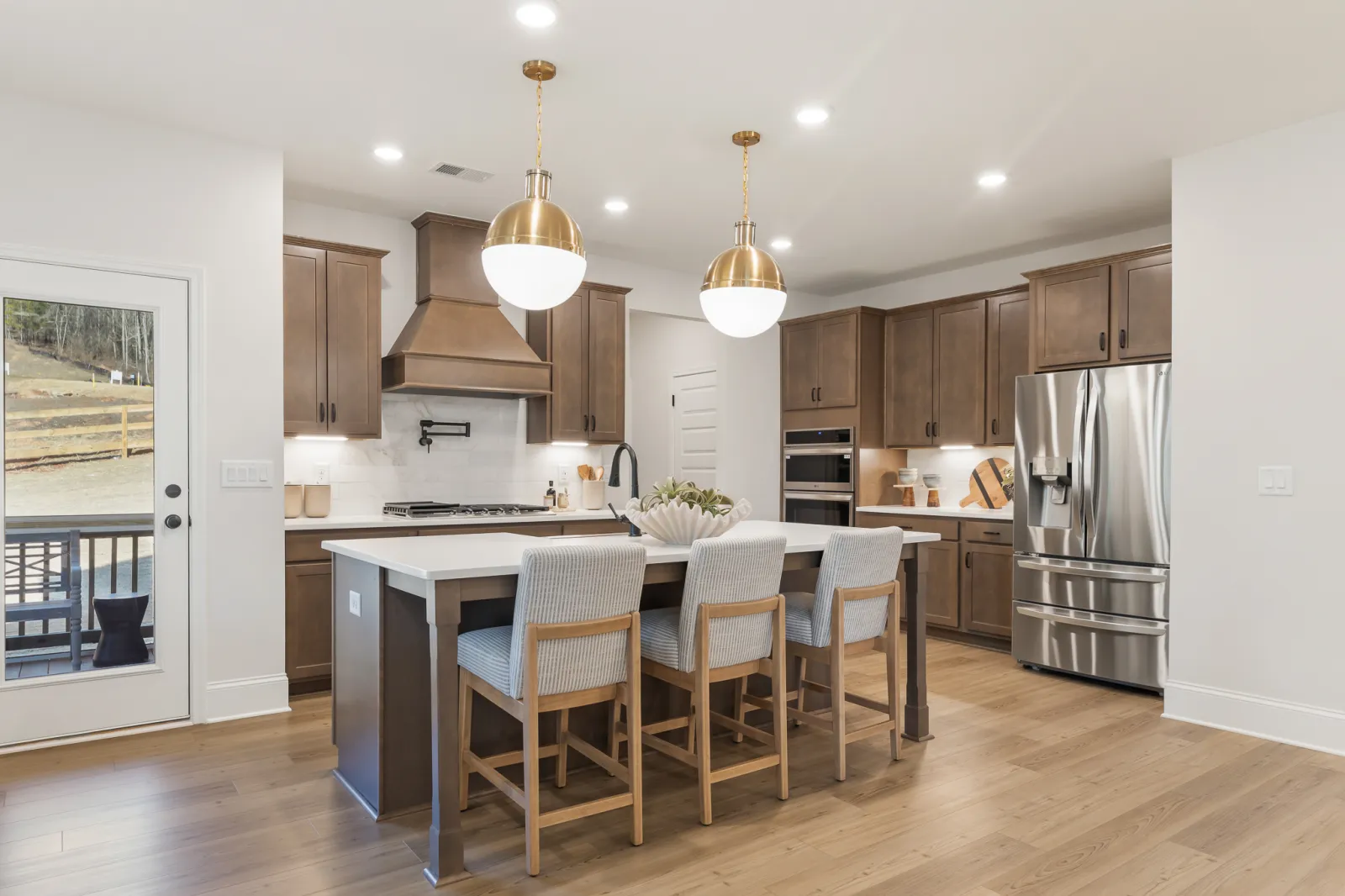 Modern kitchen with wood cabinets, stainless steel appliances, white island, and gold pendant lighting over seating area.