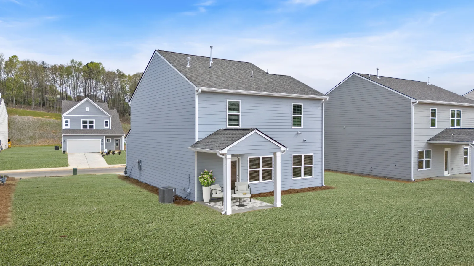 Modern gray house with porch in a suburban neighborhood under a clear blue sky.