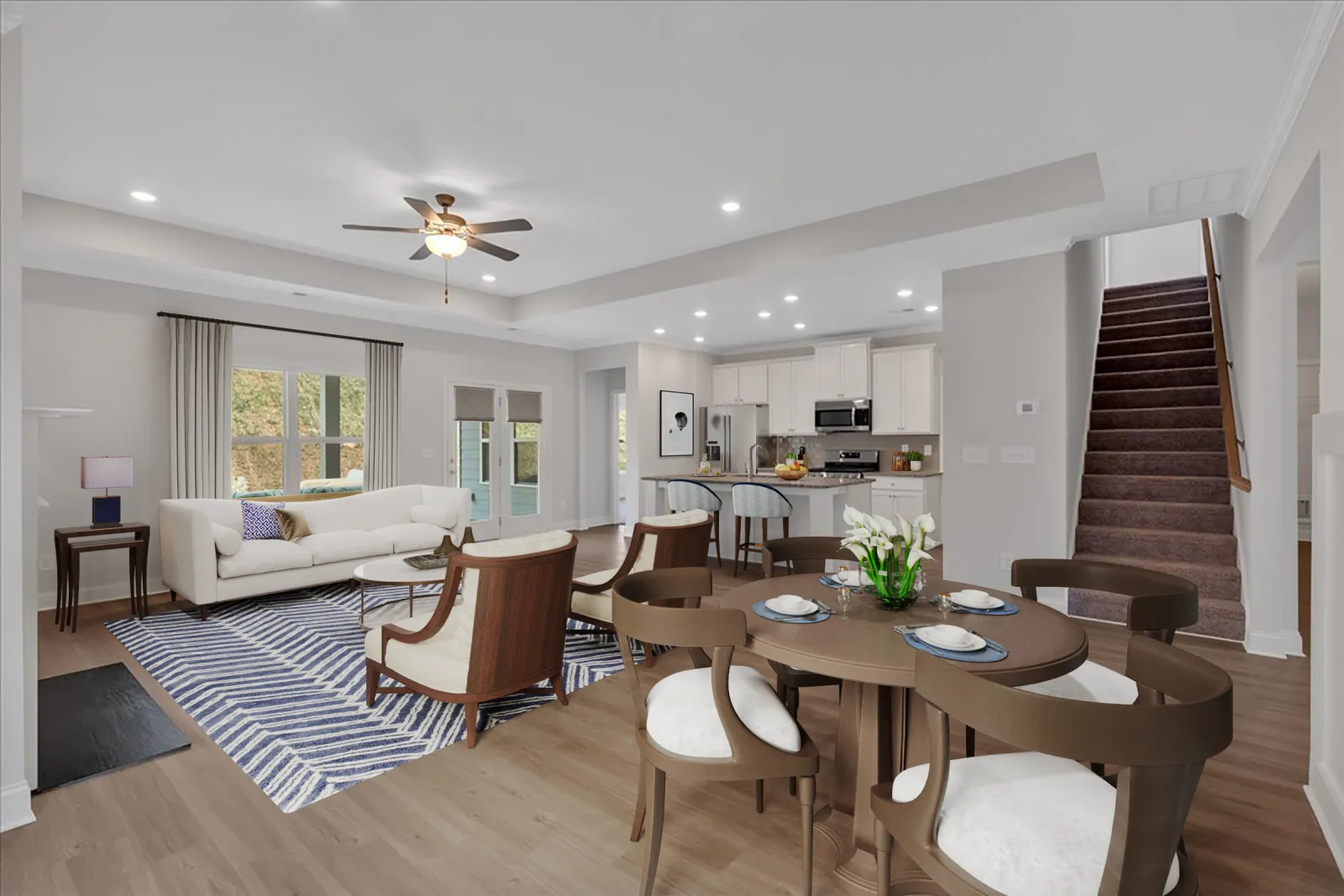Spacious open-plan living and dining area with modern kitchen, wooden floors, white walls, and staircase leading upstairs