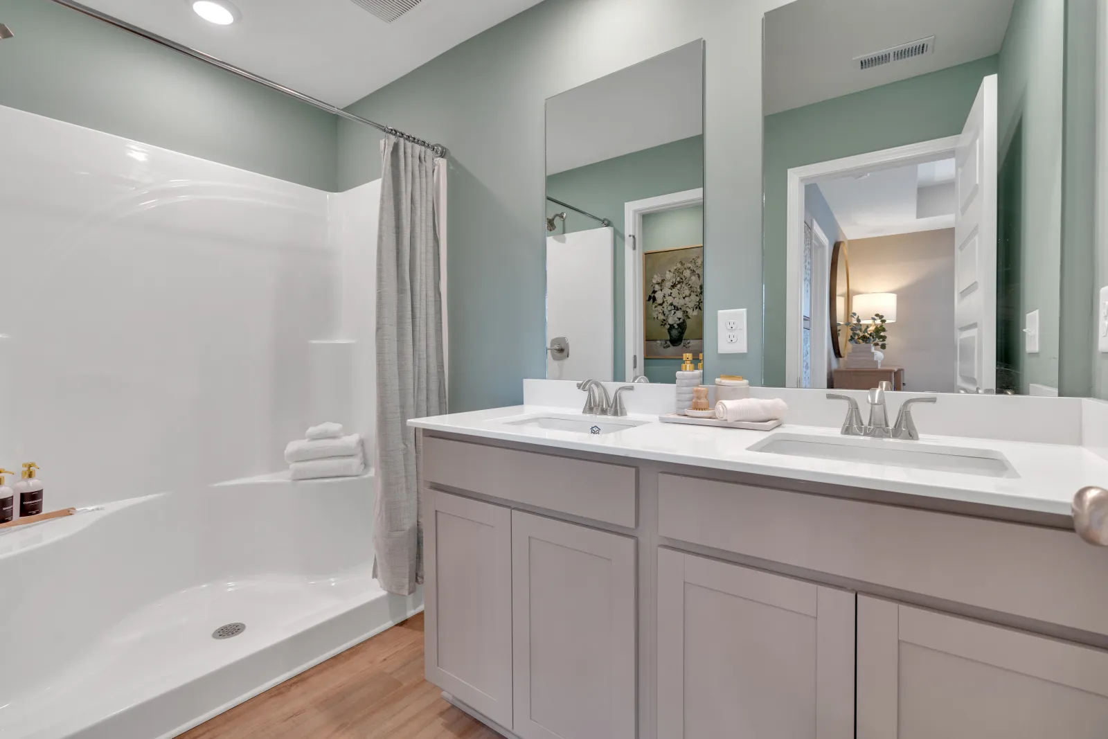 Bright and modern bathroom featuring a spacious shower, dual sinks, and light green walls.