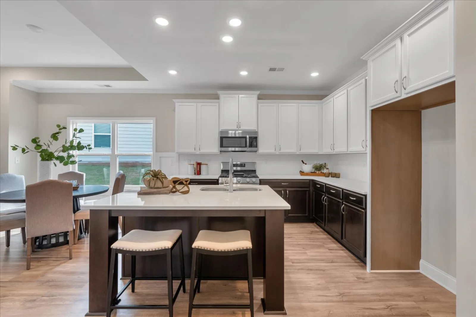 Modern kitchen with white upper cabinets, dark lower cabinets, island with stools, and hardwood floors