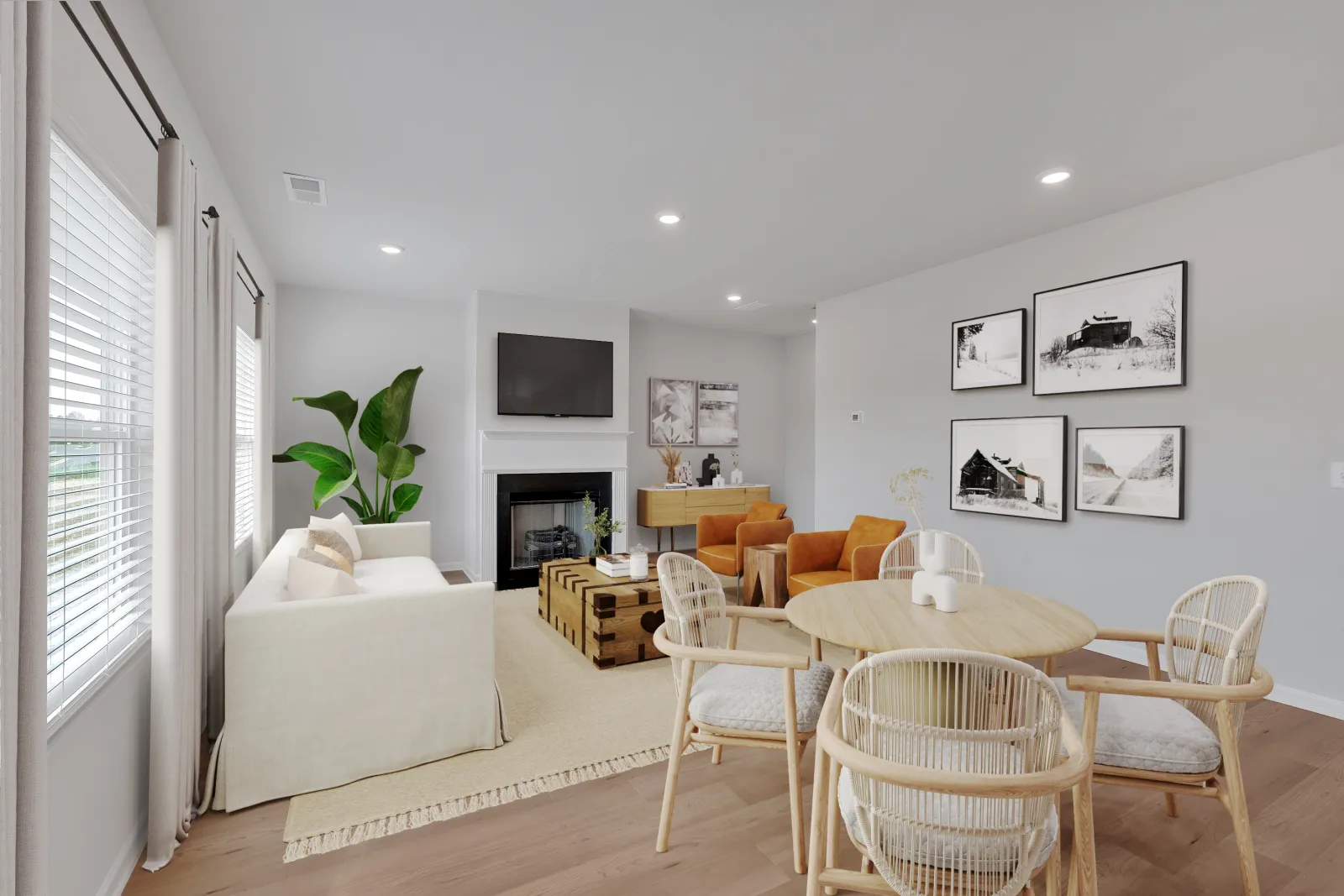 Bright modern living room with white sofa, wooden dining table, orange chairs, and fireplace under TV.