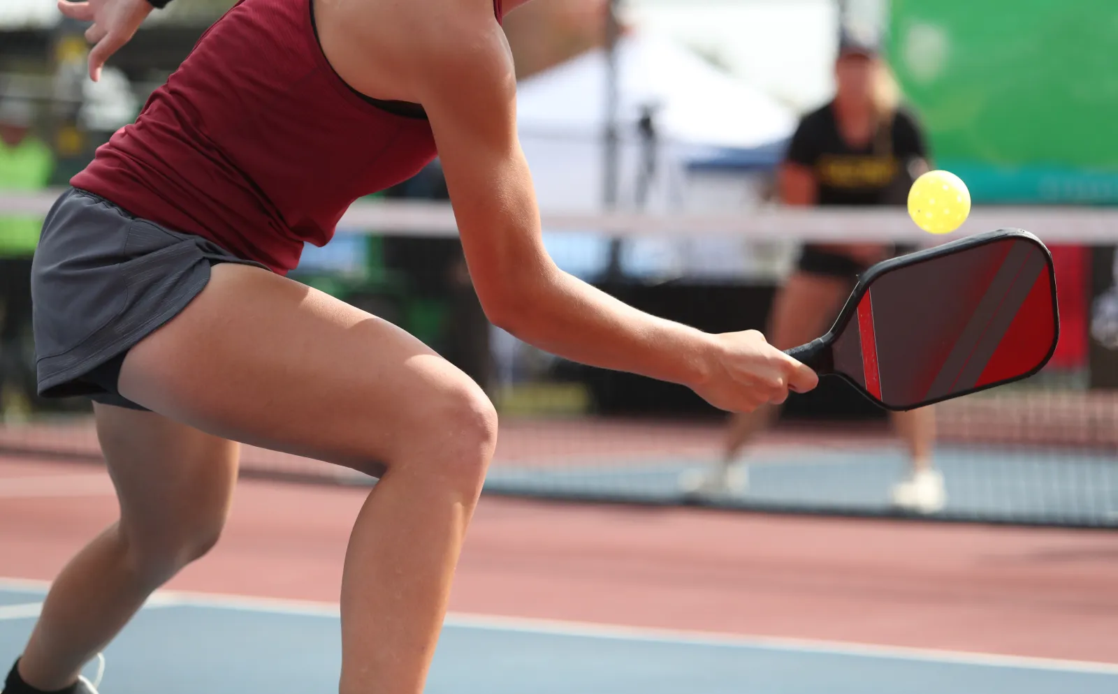Player in red shirt and black shorts hitting a yellow pickleball with a paddle on an outdoor court.