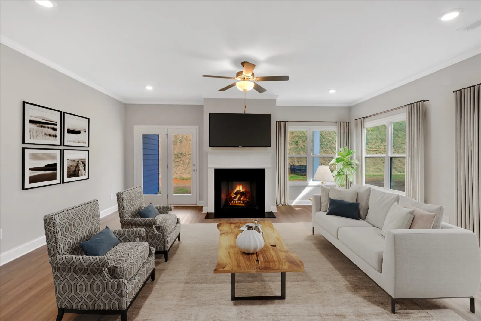 Bright modern living room with patterned chairs, white sofa, wooden coffee table, fireplace, and ceiling fan.