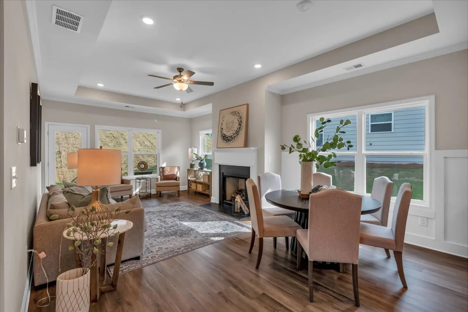 Modern living and dining area with wood floors, neutral furniture, large windows, and ceiling fan lighting.