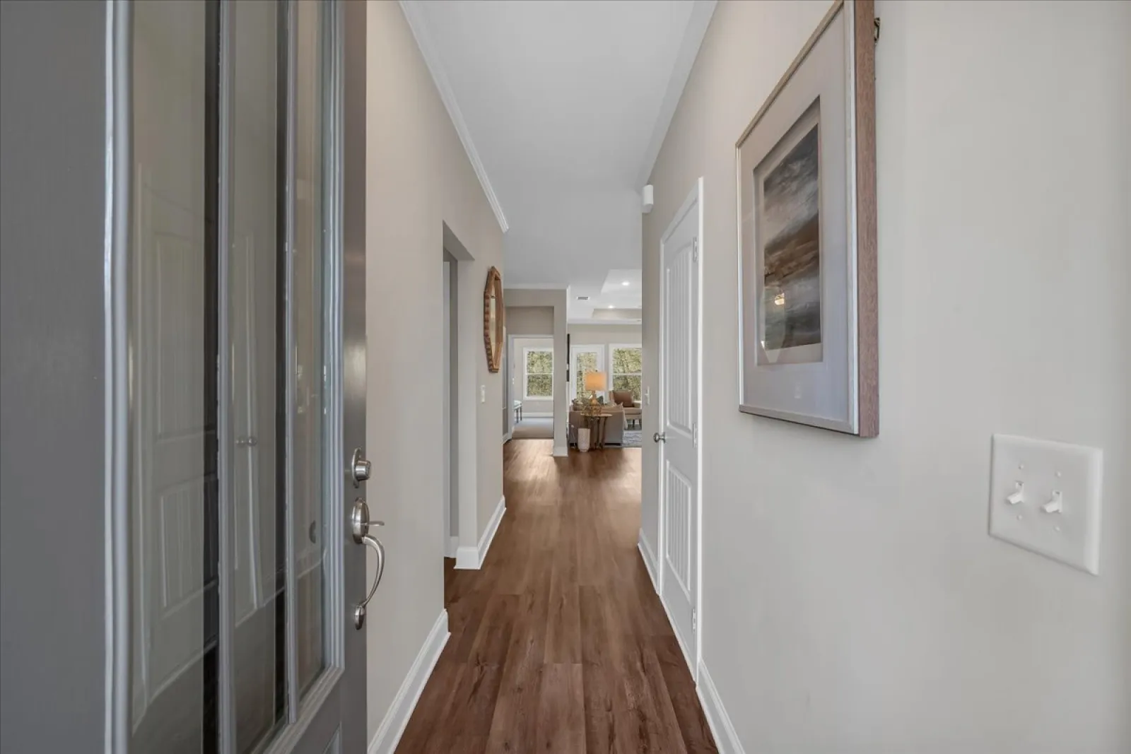 View of a modern hallway with wood flooring, neutral walls, a wall painting, and a glimpse into a living room area