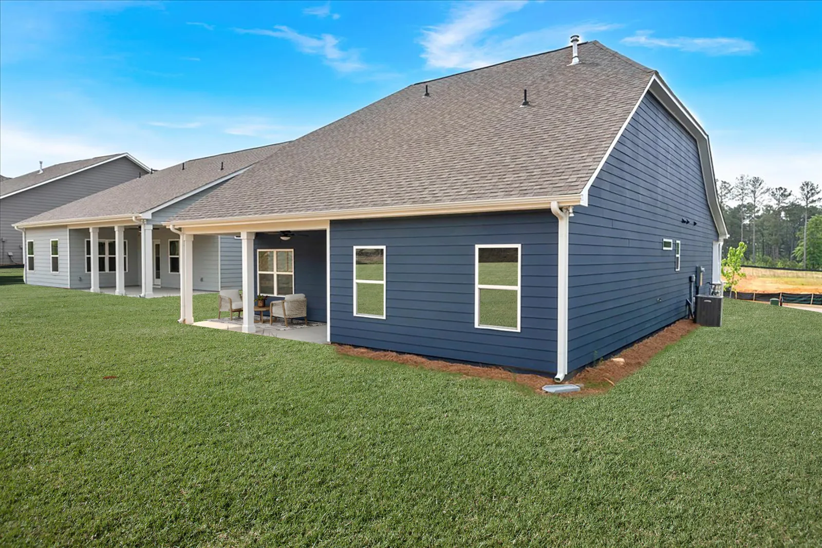 Modern blue house with a covered back patio and well-maintained green lawn under a clear sky