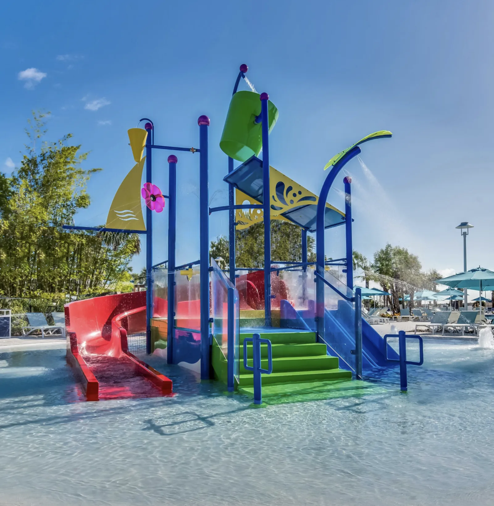 Colorful children's water playground with slides, splash features, and tipping bucket in a shallow pool on a sunny day.