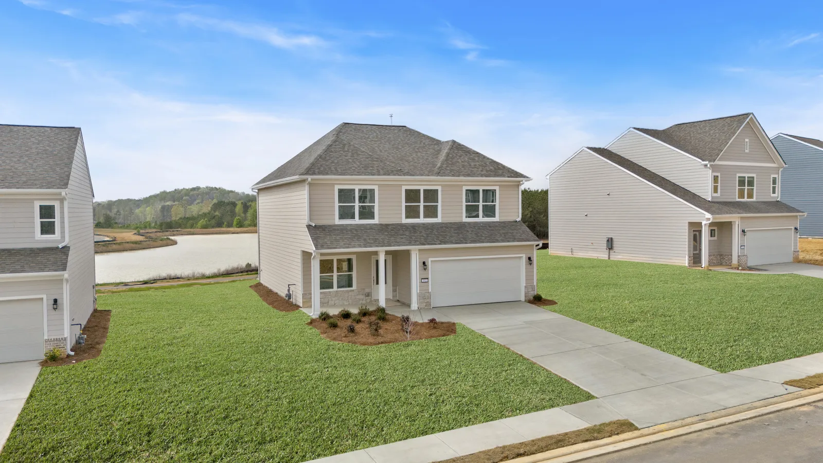 Newly built two-story house with a garage and large green lawn in a suburban neighborhood near a lake.