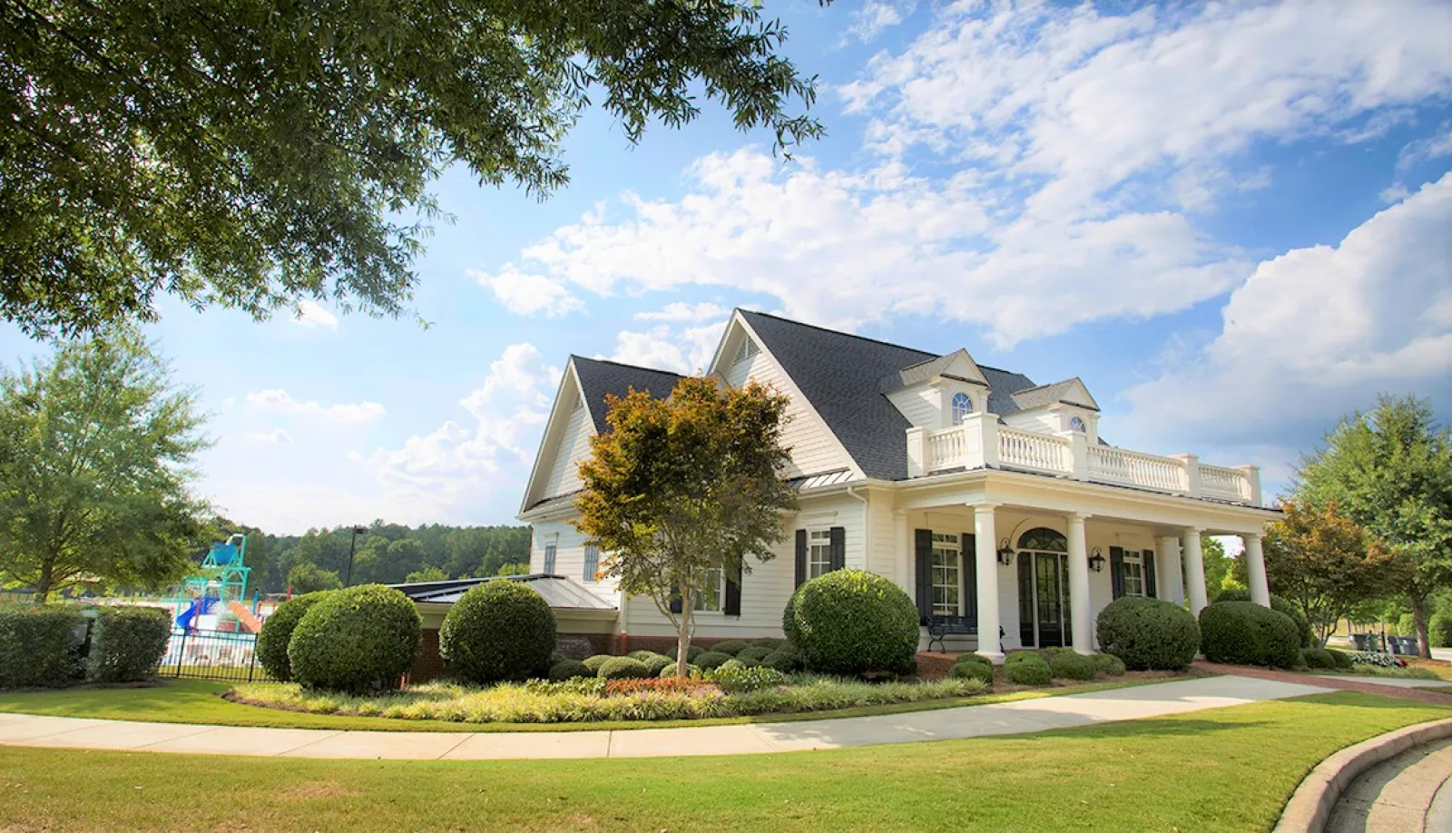 White colonial-style house with manicured bushes, lawn, and blue sky with clouds on a sunny day