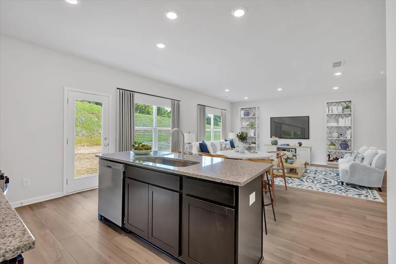 Modern open concept kitchen and living room with dark island, hardwood floors, and bright windows