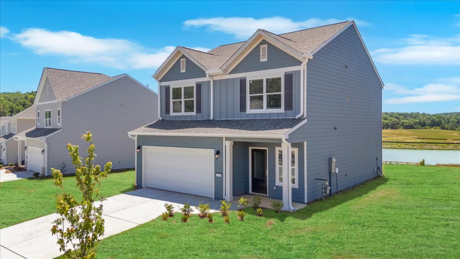 Modern two-story blue house with attached garage and manicured lawn under blue sky near a lake.