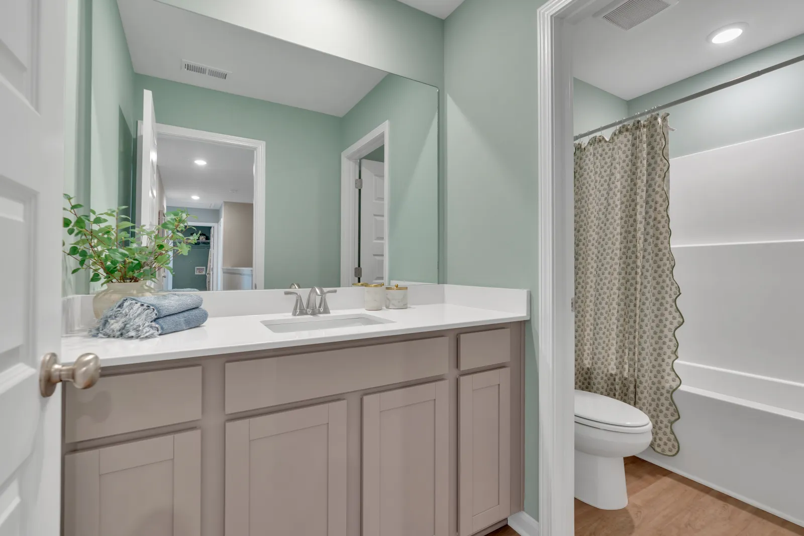 Modern bathroom with light green walls, white vanity, and elegant shower curtain.