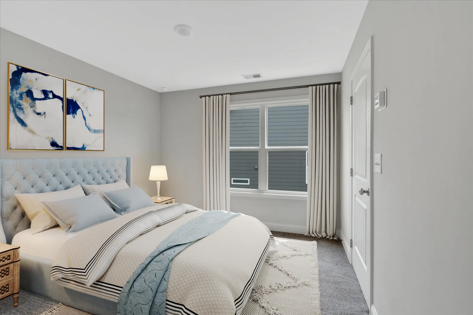 Bright bedroom with a tufted blue headboard, modern bedding, a bedside lamp, and abstract wall art under soft lighting.