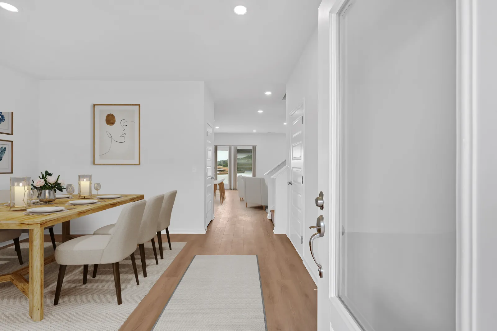 Bright modern dining area with wooden table, beige chairs, artwork, and hallway leading to living room.