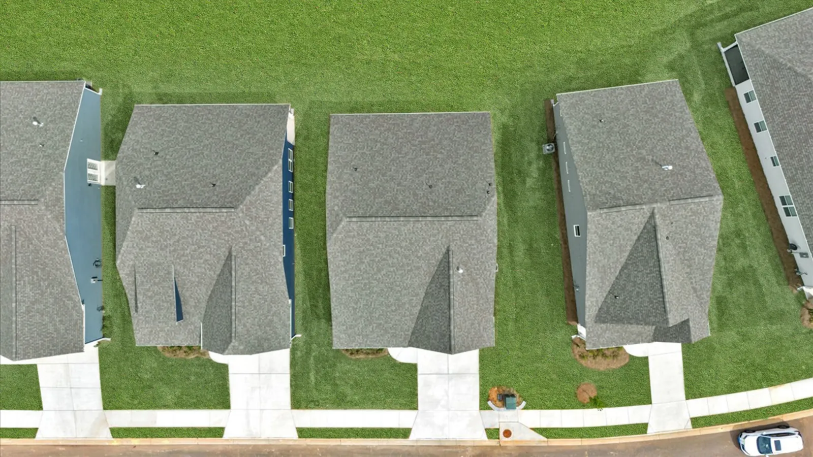 Aerial view of four suburban houses with grey roofs, green lawns, and concrete driveways in a row.
