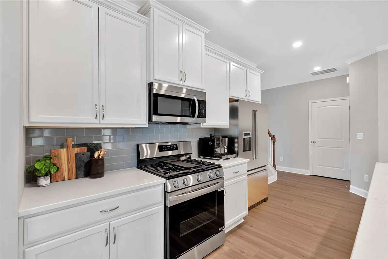 Modern kitchen with white cabinets, stainless steel stove, microwave, refrigerator, gray subway tile backsplash, and wooden floor.