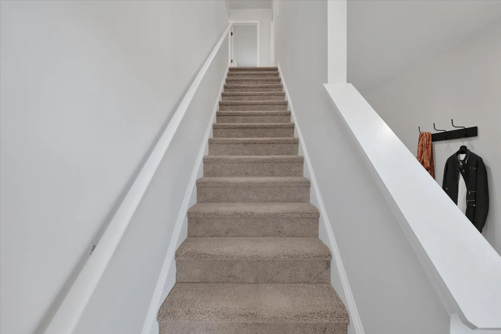 Carpeted staircase with white handrails and walls leading up to a closed white door in a bright interior.
