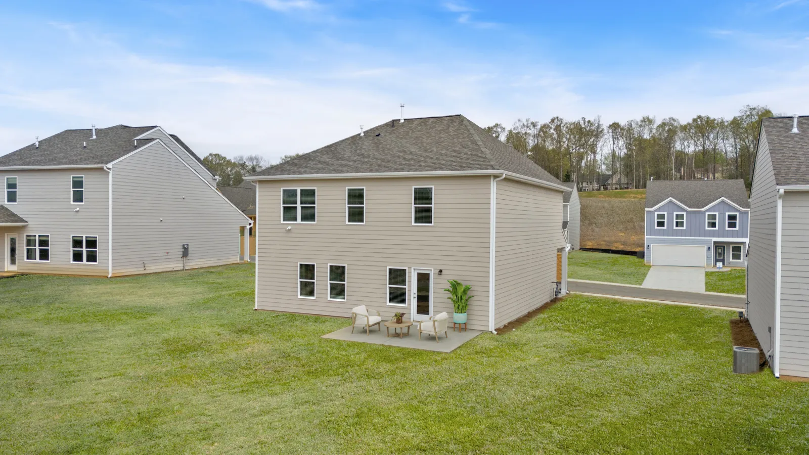 Backyard view of beige two-story house with patio furniture on green lawn and neighboring homes