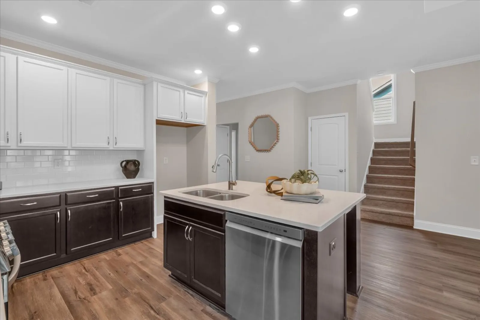 Modern kitchen with two-tone cabinetry, kitchen island with sink, stainless steel dishwasher, and wooden flooring.