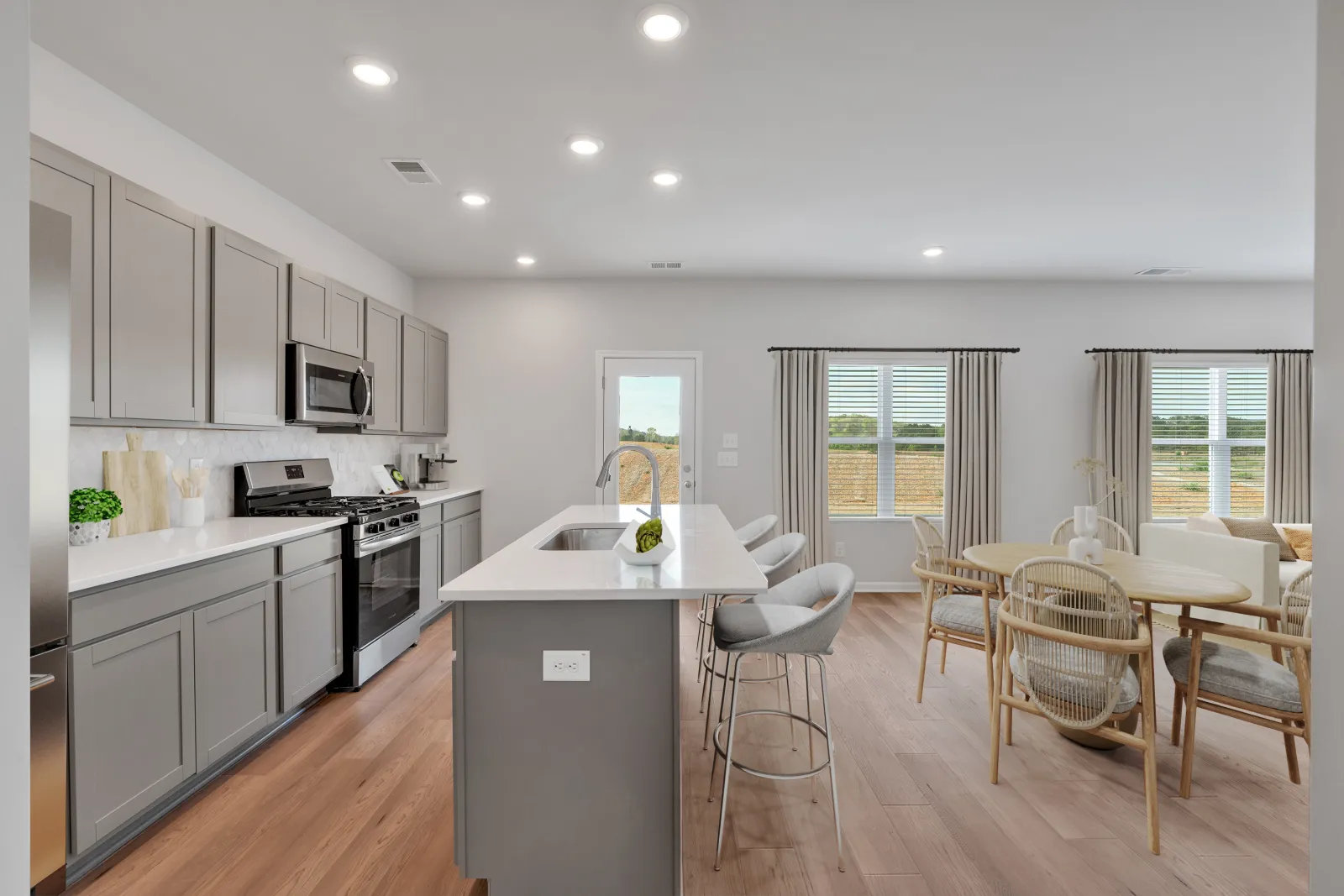Modern kitchen with gray cabinets, white island, stainless steel appliances, and adjacent dining area with wooden chairs.