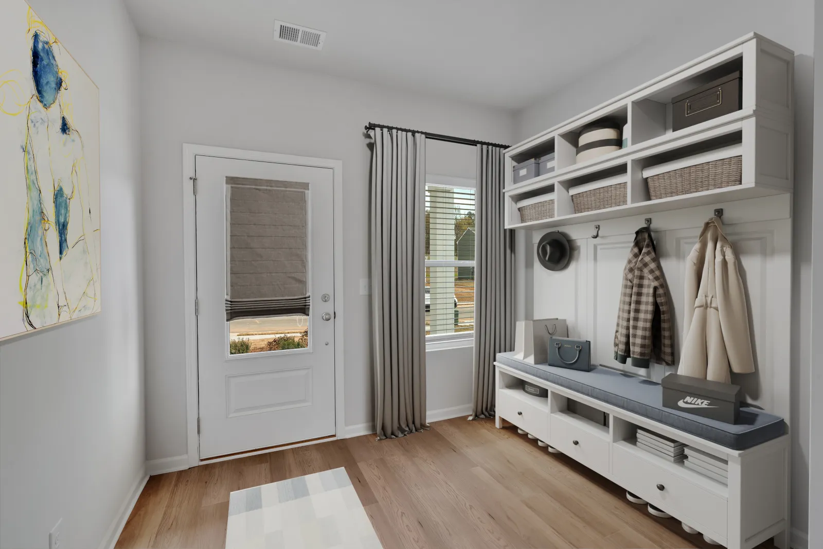 Modern mudroom with white storage bench, hooks, baskets, coats, window with curtains, and abstract wall art.