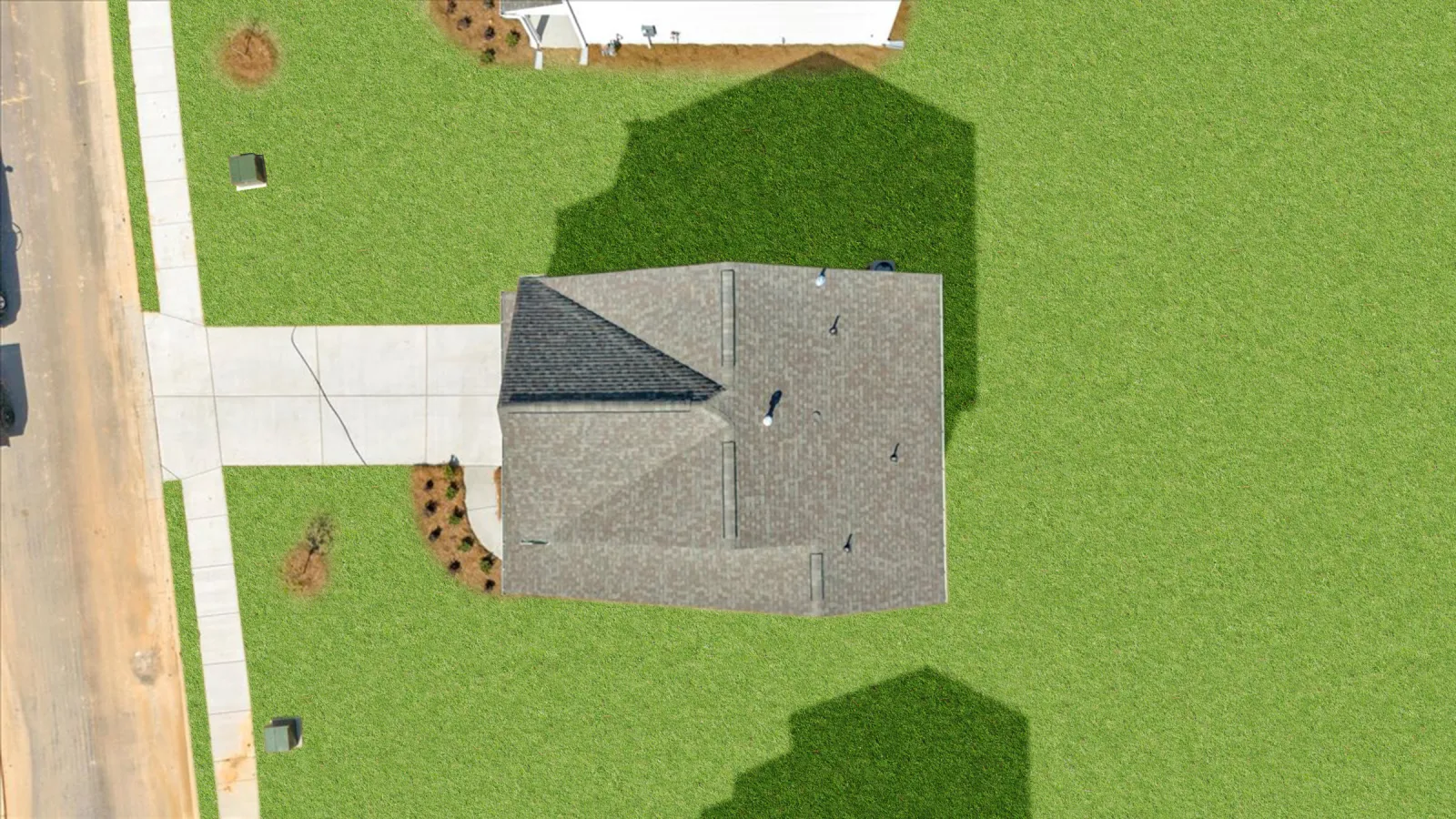 Aerial view of a single house with a gray roof, concrete driveway, and green lawn on a sunny day.