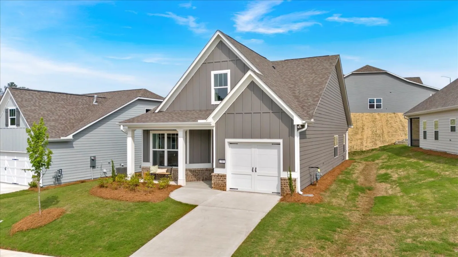 Modern gray house with a front porch, single garage, and landscaped yard under a blue sky.