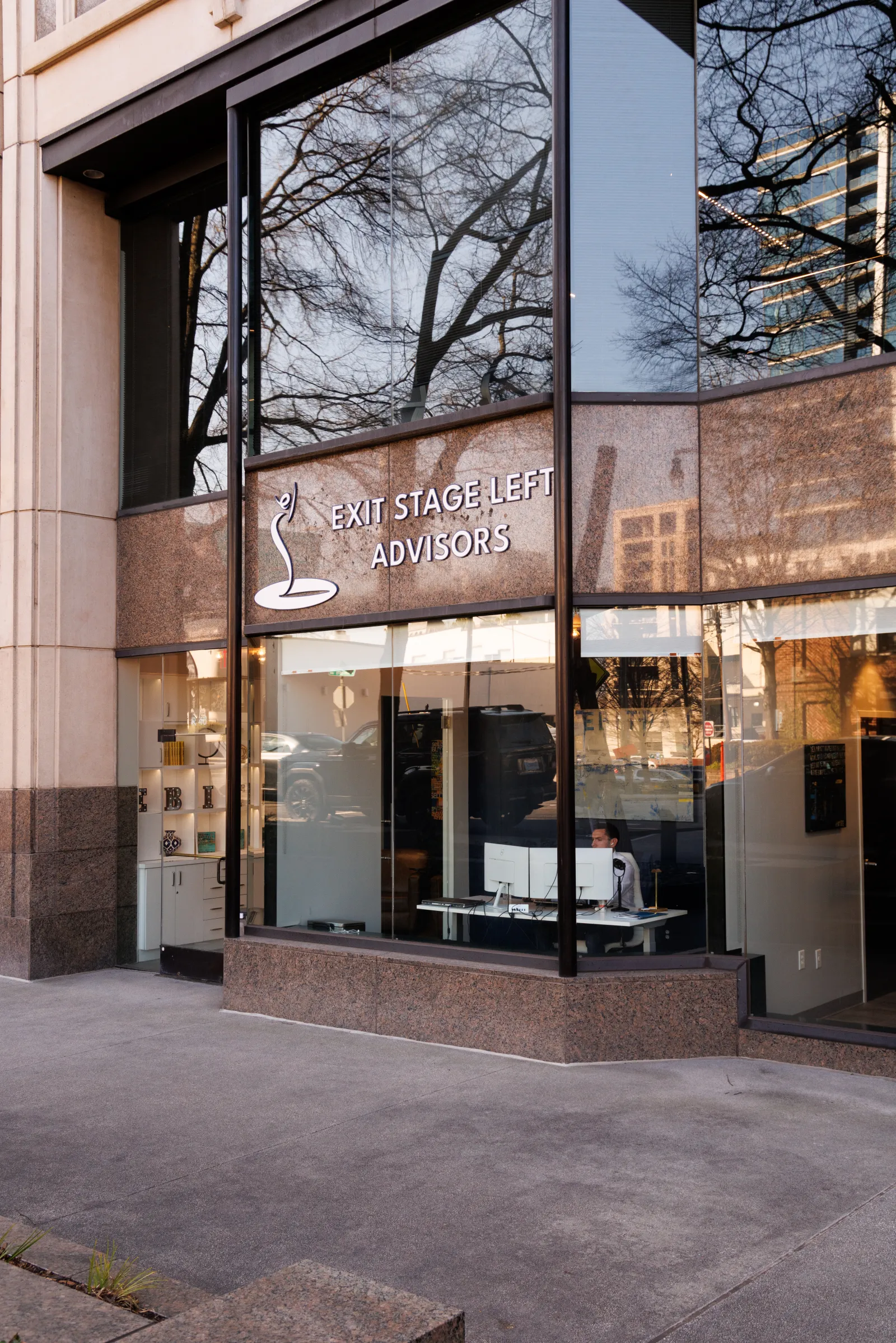 Modern office building exterior with large glass windows and EXIT STAGE LEFT ADVISORS sign.